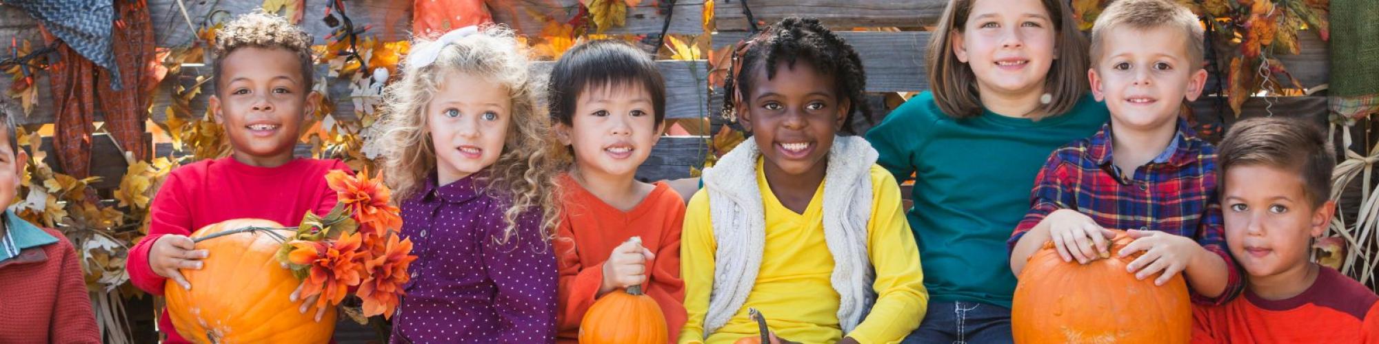 children holding pumpkins with a fall background